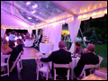 Wedding guests sitting at their tables in a wedding tent with clear ceiling and rope lights, next to the dance floor and cupcake tower